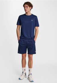 Granatowe spodenki sportowe i dopasowana koszulka z krótkim rękawem wykonane z lekkiego materiału, z małym białym logo na klatce piersiowej i spodenkach.