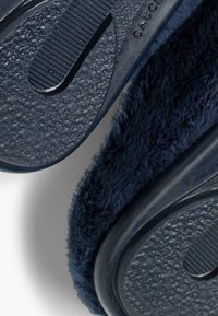 Mornarsko modri copati z mehko, puhasto teksturo in gumijastimi podplati, ki imajo vzorce za oprijem. Zaobljena oblika za udobje.