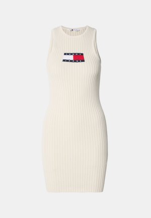 Ženské telové šaty s rebrovanou textúrou v krémovej farbe, vysokým výstrihom a bezrukávovým dizajnom. Obsahujú kontrastnú logo nášivku na hrudi.