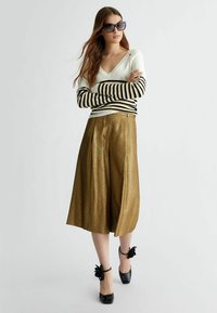 Maglietta a maniche lunghe bianca e nera a righe abbinata a pantaloni larghi dorati lucenti, completata da tacchi neri decorati con accenti floreali.