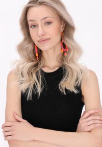 Svart ärmlös topp med ett texturerat mönster. Bär färgglada, pärlade hoops med örhängen i rosa, orange och gulddetaljer. Långt blont hår.