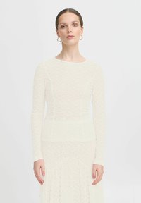 Haut de robe en dentelle ivoire à manches longues, dot�é d'un design ajusté, d'un col rond et d'un motif texturé, superposé à une jupe fluide.
