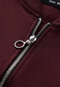 Bordeaux sweatshirt med en sølv metal lynlås, ribbet krave og et rent udtryk. Lynlåsens træk har en cirkulær tab for nemt greb.