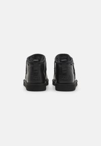 Botas de cuero negras hasta el tobillo con forro suave, suela de goma plana y tira de marca en el talón. Presenta un panel lateral texturizado y una pestaña trasera para tirar.