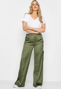 Olijfgroene satijnen cargobroek met een hoge taille, wijde pijpen en twee zijzakken, gecombineerd met een plain witte V-hals t-shirt en sneakers.