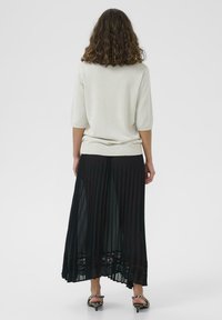 Svetlo šedý pletený top s trojštvrťovými rukávmi, skombinovaný s čiernou plisovanou sukňou so čipkovým lemom na spodnom okraji. Doplnkované obuvou na podpätku.