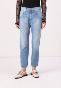 Vaqueros de mezclilla de un azul claro con un diseño de pierna recta, cintura alta y estilo clásico de cinco bolsillos. Llevados con zapatos de tacón abiertos en color beige.