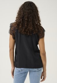 Black top with short lace sleeves, smooth fabric, relaxed fit, featuring intricate floral lace detailing on shoulders, paired with light jeans.