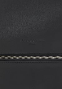 Sac en cuir noir avec une surface texturée, un nom de marque embossé et un détail de fermeture éclair en argent. Design minimaliste avec une apparence épurée.