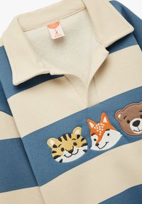 Light blue and beige striped polo shirt featuring embroidered animal faces: a tiger, fox, and bear. Soft fabric with a collar.