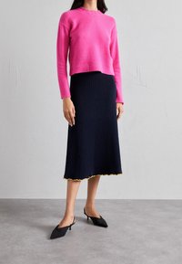 Różowy, krótki sweter o prążkowanej fakturze; granatowa spódnica do kolan z pionowymi prążkami i żółtym falistym brzegiem; czarne buty na obcasie z ostrym noskiem.