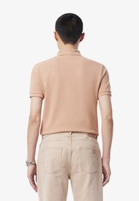 Vaaleanpunainen polo-paita, jossa on lyhyt kaulus ja lyhyet hihat, sekä sileä pinta, yhdistettynä vaaleisiin farkkuihin.