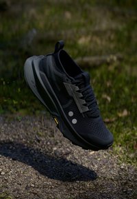 Black athletic shoe with a textured upper, reflective accents, and a thick, cushioned sole featuring a yellow detail on the outsole.