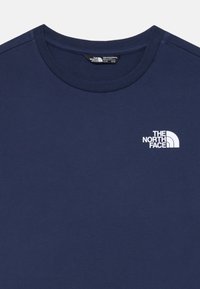 Camiseta de algodón color azul marino con cuello redondo. Presenta un logo blanco en la parte izquierda del pecho. Textura suave, diseño casual.