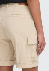 Kaki cargo shorts med rullet kant, flere lommer og et teksturert stoff. Bak på livet er det et merket lærmerke.