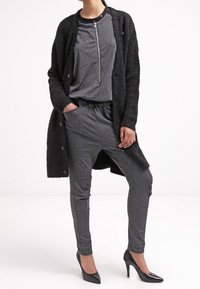 Grå, stickad cardigan med en strukturerad yta, bärs över en grå zip-up topp och grå tapered byxor. Svarta högklackade skor fullbordar outfiten.