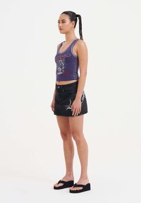 Canotta grafica viola con gonna mini in denim nera caratterizzata da un motivo ricamato di rondini, abbinata a flip-flop neri con piattaforma.