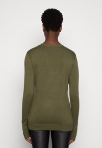 Maglione lungo verde oliva a maniche lunghe in morbido tessuto lavorato a maglia con scollatura tonda e polsini a coste. Silhouette aderente con una texture liscia.