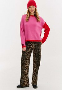 Jasnoružový a červený oversize sveter s dlhými rukávmi, skombinovaný s nohavicami s leopardím vzorom a širokými nohavicami. Textúrovaná látka a ležérny strih.
