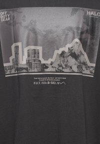 Grå t-shirt med en grafik av ett berg och en stadsbild i svart och vitt, med texten "OFF DUTY GEAR" i fetstil högst upp och produktdetaljer nedanför.