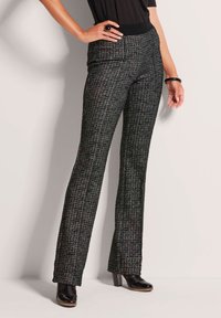 Zwarte en grijze textielbroek met een gestructureerde, patroonafwerking. Tapered fit, flared benen en gedragen met zwarte hoge hakken.