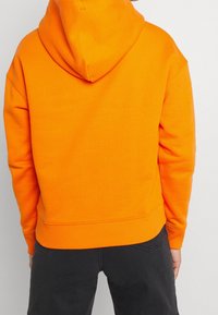 Sudadera con capucha de color naranja brillante hecha de mezcla de algodón, con bolsillo tipo canguro, puños y dobladillo acanalados. Incluye una capucha espaciosa.