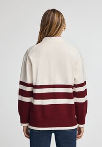 Stickad tröja i grädde med vinröda och vita horisontella ränder, med krage och ribbad mudd och nederkant.