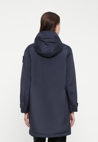 Parka blu navale con cappuccio, caratterizzata da una linea dritta, maniche lunghe e accessori regolabili ai polsini. Tessuto morbido e leggero.
