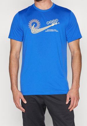 Mand iført en blå t-shirt med et gult mekanisk tandhjulsdesign og tekst "just do it" og "spotting you since seventy two."