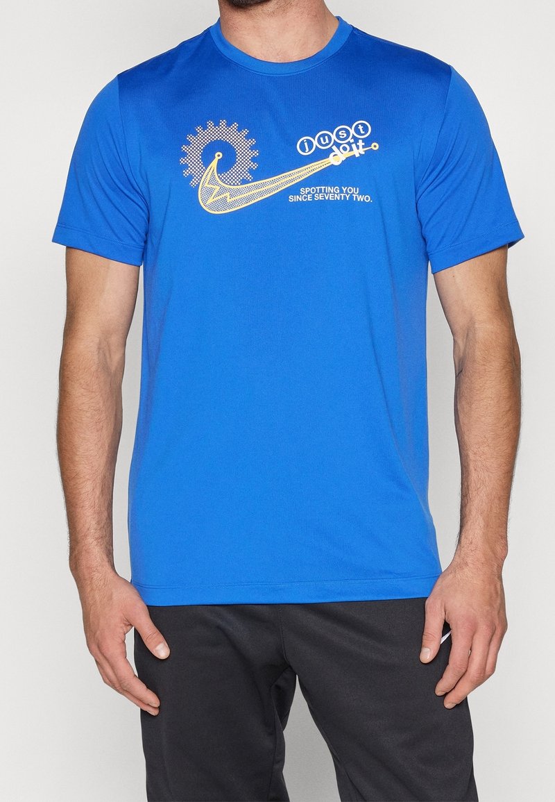Homme portant un t-shirt bleu avec un motif d'engrenage mécanique jaune et le texte "just do it" et "spotting you since seventy two."