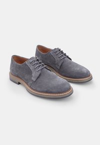Scarpe oxford in suede grigio con punta arrotondata, design con lacci, suola in pelle marrone a contrasto e cuciture visibili lungo i bordi.