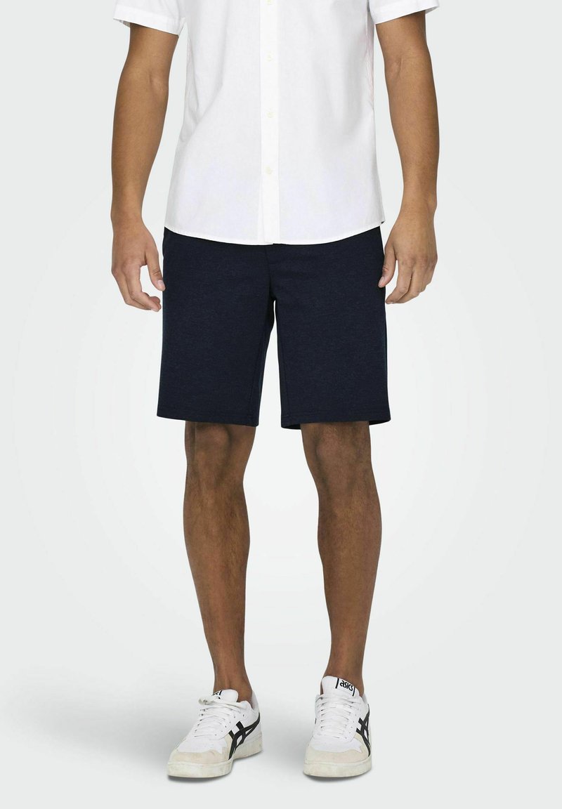 Marineblauwe katoenmix korte broek met een rechte snit, zijzakken en een subtiele textuur, gecombineerd met een wit T-shirt met korte mouwen en sneakers.