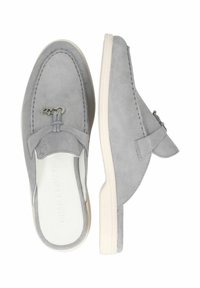Des chaussures en daim gris à enfiler avec une semelle en caoutchouc blanche, rehaussées par une sangle décorative et du matériel en métal, présentant des détails cousus.
