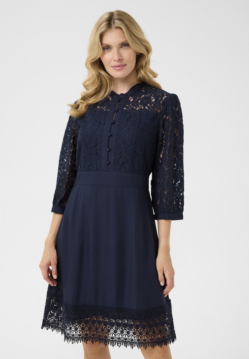 Navy dress featuring a lace bodice and three-quarter sleeves, with button detailing and a lace hem, creating a textured and layered design.