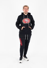 Zwarte sport hoodie met rood San Francisco 49ers logo, gecombineerd met zwarte joggerbroeken met de rode tekst "49ers", beide gemaakt van een katoenmix.