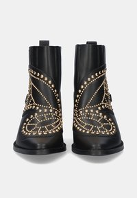 Botas de tobillo negras de cuero con un diseño de tachuelas doradas, textura suave y punta redonda. La parte trasera incluye una lengüeta para facilitar el calce.