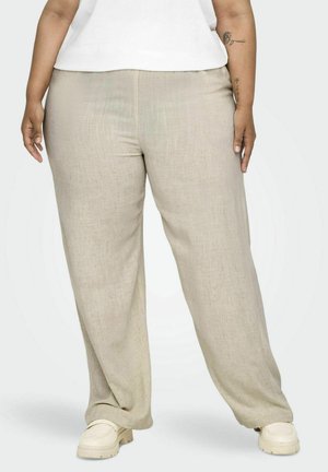 Pantalon en lin beige clair avec une coupe décontractée, présentant une texture lisse et des jambes larges, associé à des chaussures à enfiler de couleur claire.
