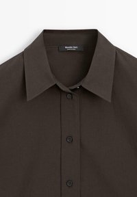 Dunkelbraunes Hemd mit Knopfleiste und klassischem Kragen. Verfügt über eine glatte Textur und schwarze Plastikknöpfe. Das Etikett trägt die Aufschrift "Massimo Dutti".