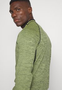 Groene, lange mouwen sportshirt in een textuurmix, met een zwarte accentnaad en een logo op de kraag in felgeel.