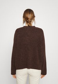 Hnědý pletený svetr s volným střihem, má kulatý výstřih a dlouhé rukávy, vyrobený z měkké, texturované tkaniny.