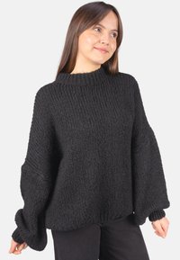 Grober schwarzer Strickpullover mit hohem Kragen, weiten Ärmeln und lockerem Sitz. Auffälliges strukturiertes Muster durchgehend.