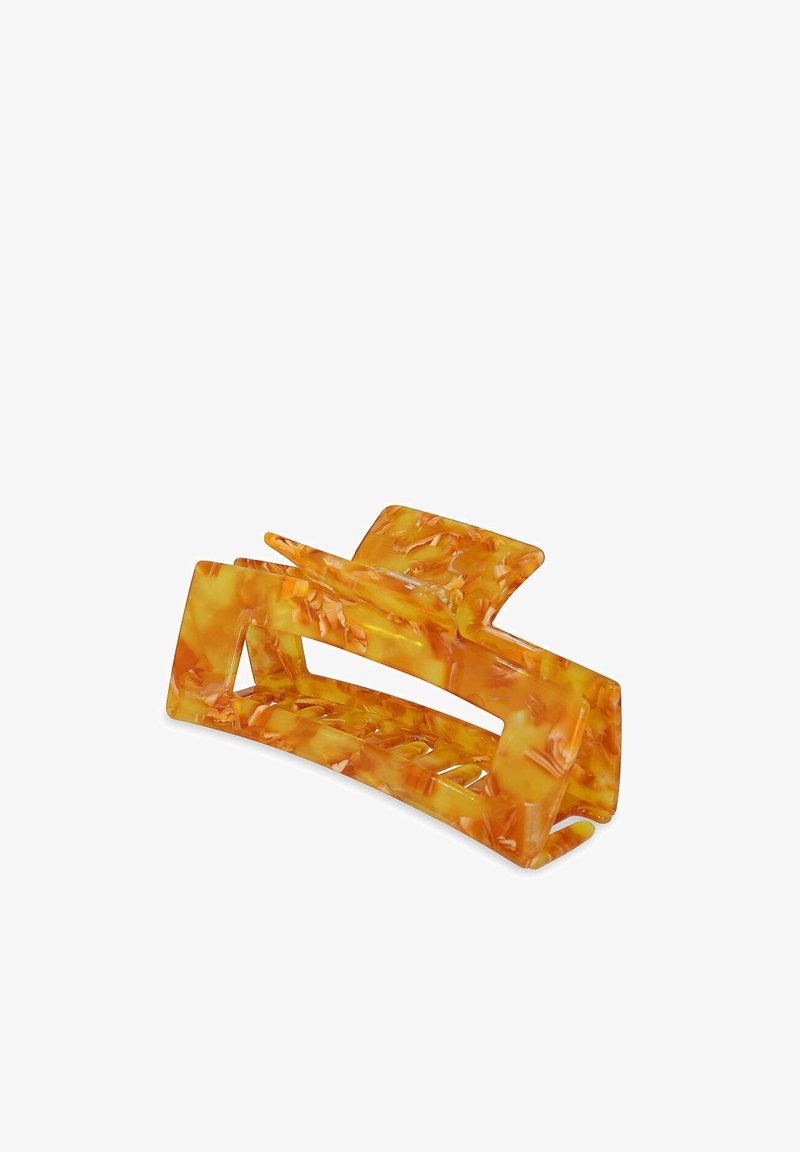 Une pince à cheveux orange translucide en plastique, présentant un motif marbré, des découpes rectangulaires et une texture lisse.