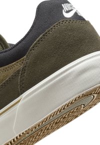 Zaļi zamša un tumšas auduma sporta apavi ar baltu gumijas zoli, ar teksturētām detaļām un izteiktu logo augšpusē.