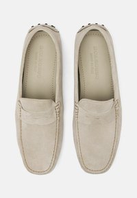 Bež antilop loafers s pro�šivenom, glatkom površinom i zaobljenim vrhom. Ima ukrasno gornje šivanje i male crne metalne naglaske.