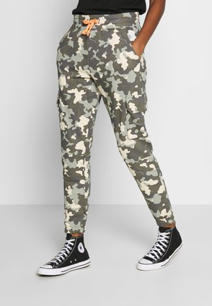 Person wearing gray and beige camouflage cargo pants with an orange drawstring and black high-top sneakers with white laces.
