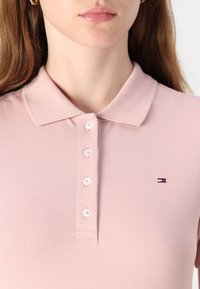 Ανοιχτό ροζ πόλο μπλουζάκι με υφή στο ύφασμα, διαθέτει κολάρο και πέντε κουμπιά. Μικρό λογότυπο στη αριστερή πλευρά.