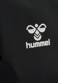 Wit gestileerd bijenlogo boven het woord "hummel" gedrukt op zwarte stof.