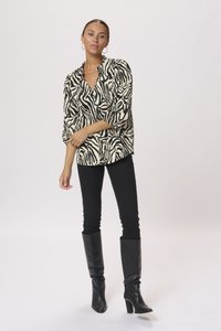 Zwart-witte blouse met zebraprint en driekwartmouwen, gecombineerd met zwarte skinny jeans en kniehoge zwarte haklaarzen.