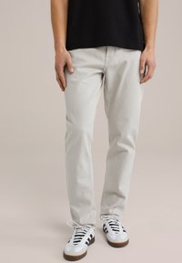 Lichtgrijze katoenen pantalons met een rechte pasvorm. Gecombineerd met zwarte veters en witte sneakers met zwarte accenten.