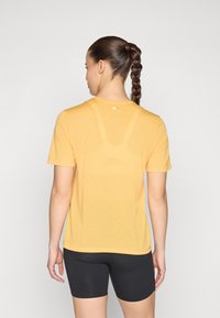 Yellow, short-sleeve athletic shirt with textured fabric, round neckline, and logo detail at the back, paired with black shorts.